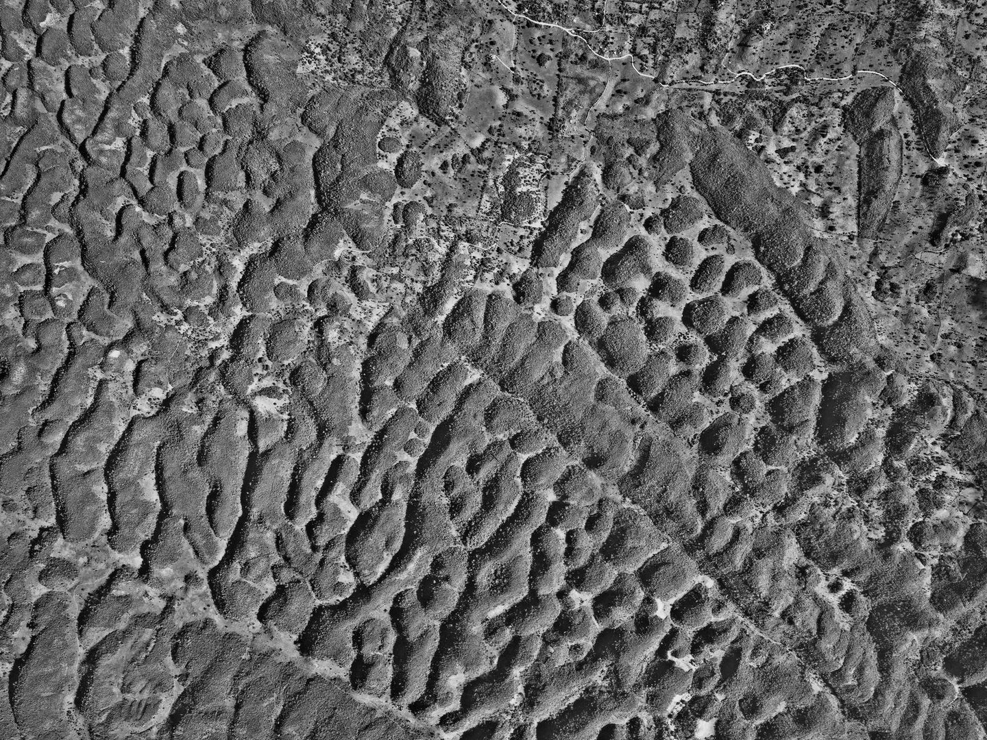 A black and white aerial photo of a limestone landscape. The limestone looks wrinkled and has created an intricate wavy pattern, with channels and areas of raised ground running at all sorts of angles across the image.