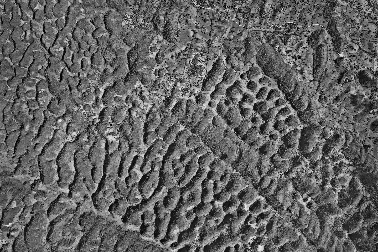 A black and white aerial photo of a limestone landscape. The limestone looks wrinkled and has created an intricate wavy pattern, with channels and areas of raised ground running at all sorts of angles across the image.