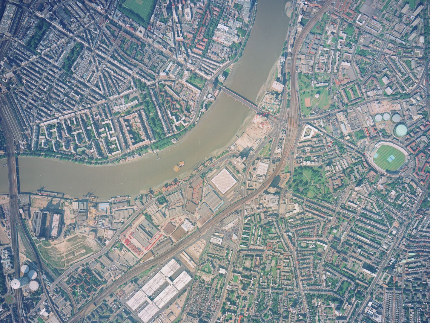 A colour aerial photo of London. A muddy River Thames runs across the top left quadrant with a railway parallel to it. Battersea Power Station is in the bottom left corner and the green of The Oval stands out at the middle of the right edge.