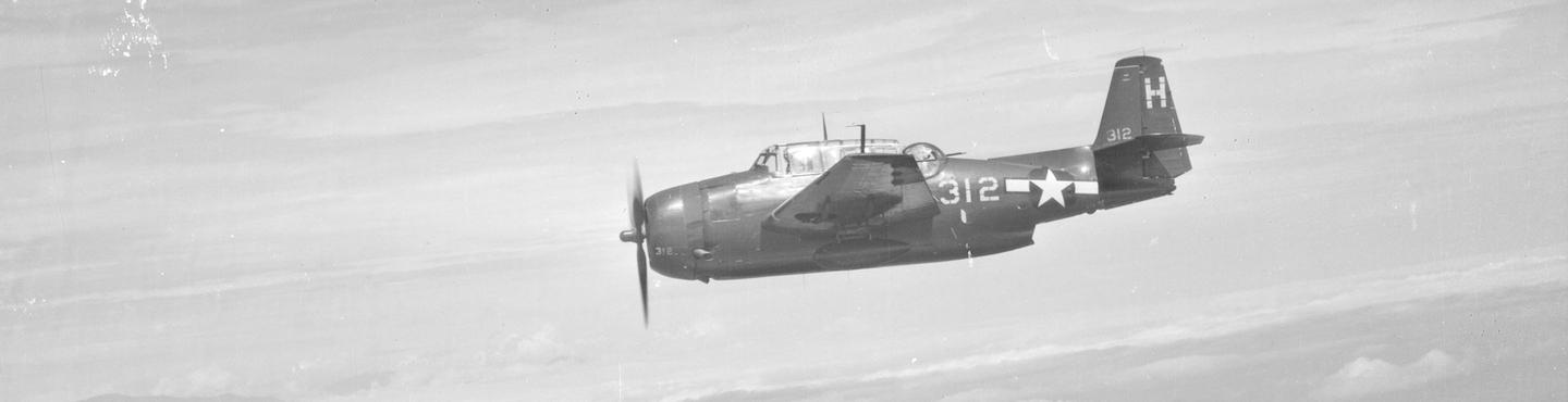 A black and white oblique aerial photo of an airborne plane from side-on. The plane has one propellor and a see-through cockpit with the pilot visible. There is a rear-facing gun turret, and the fuselage is marked with an American star and ‘312’.