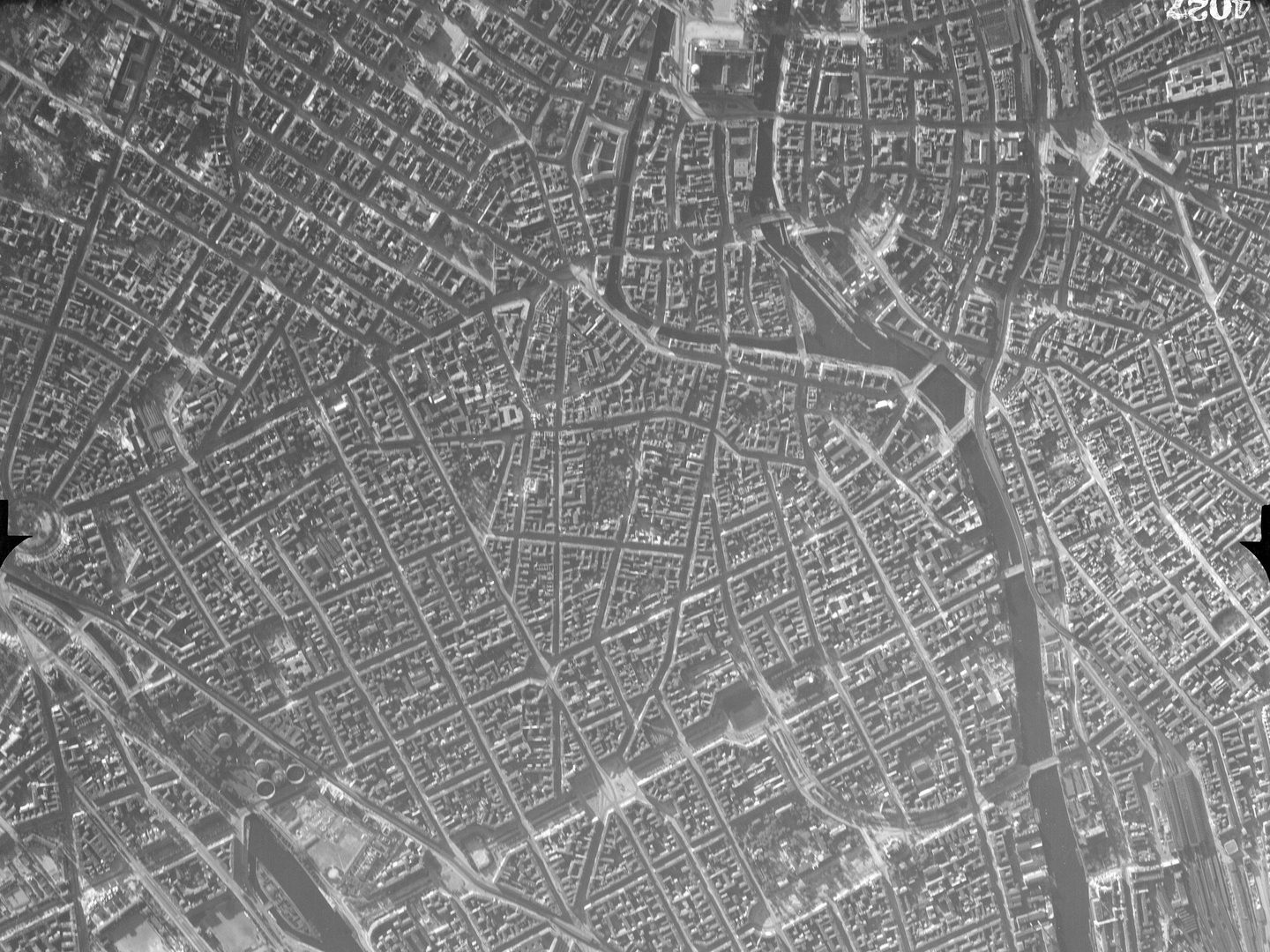 A black and white aerial photo of Berlin from a high altitude. A river runs vertically through the right side of the image, parallel with the right edge. The city buildings are arranged in a rough grid.