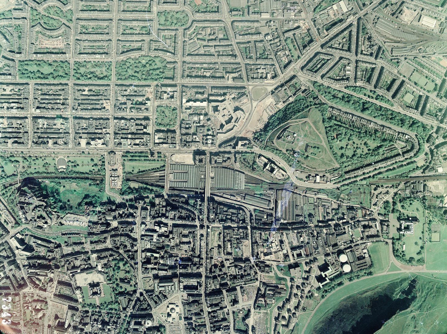 A colour aerial photo of Edinburgh, with the substantial roofs of Waverley Station in the middle. The green grass and trees of Calton Hill are right of centre. At the top is the grid of the New Town, with the more irregular Old Town at the bottom.