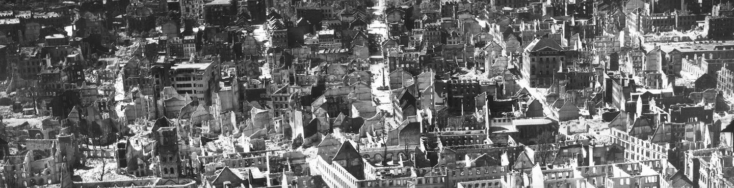 A historic black and white oblique aerial photo of a city. The city shows signs of having been heavily bombed, with many of the buildings roofless and gutted.