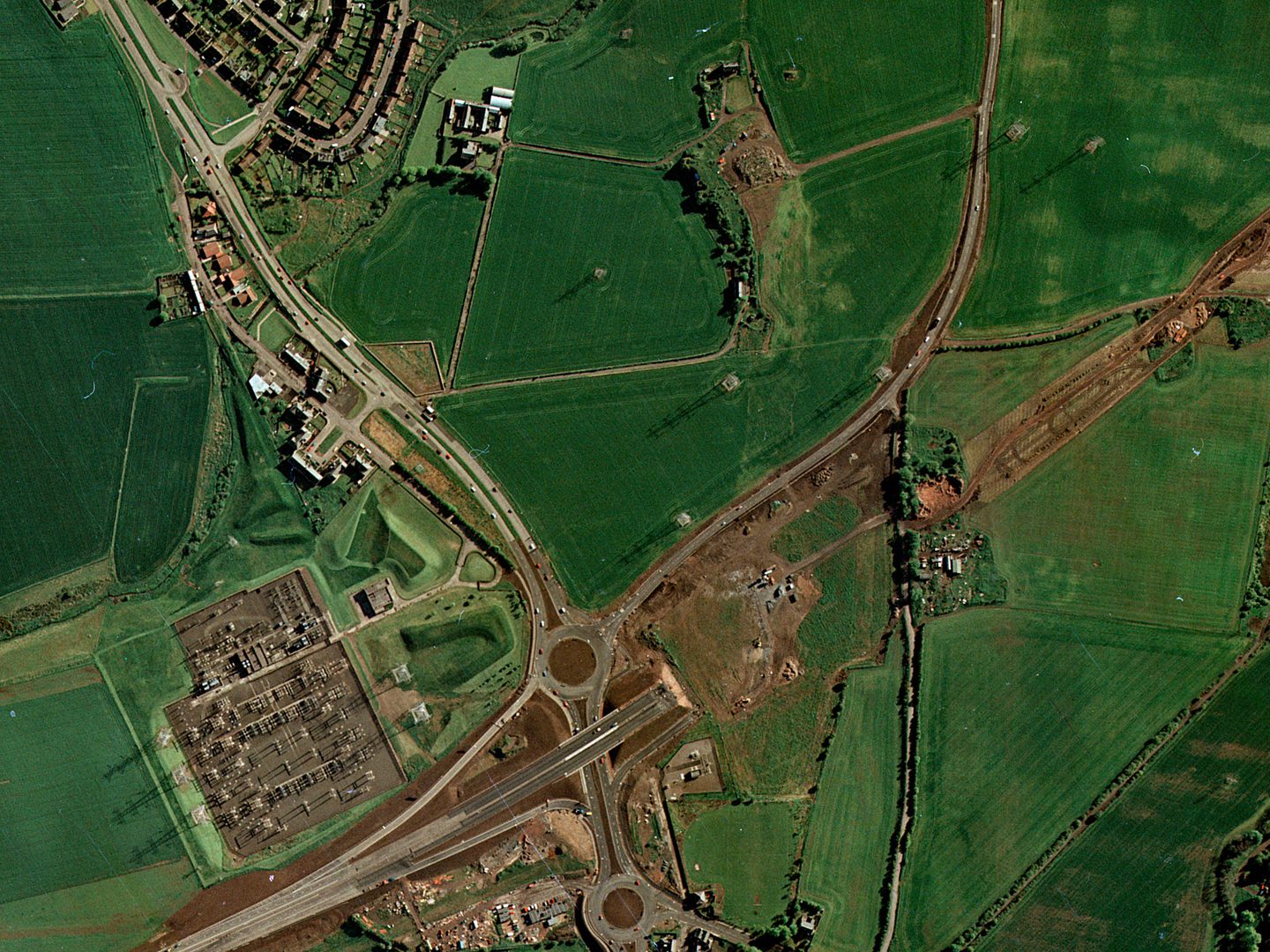 A colour aerial photo of the same scene as the last 2 images. The chimneys are still present, but the excavations are covered with fields. A major new motorway with 2 roundabouts is being constructed at the bottom of the image.