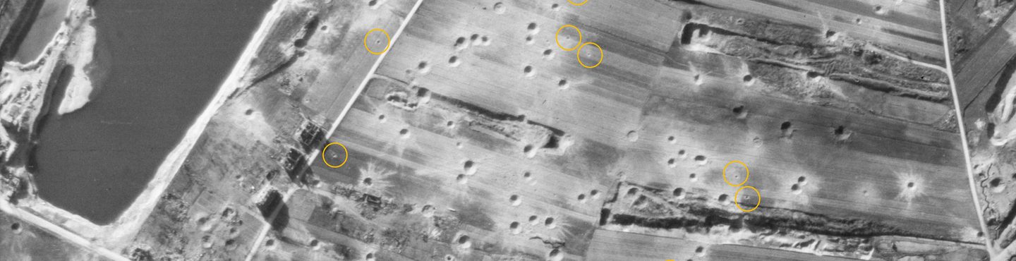 A black and white aerial photo of fields. A large pond is visible centre left. The fields are pockmarked with bomb craters. Digital yellow circles have been drawn around small dots indicating where bombs have landed but not exploded.