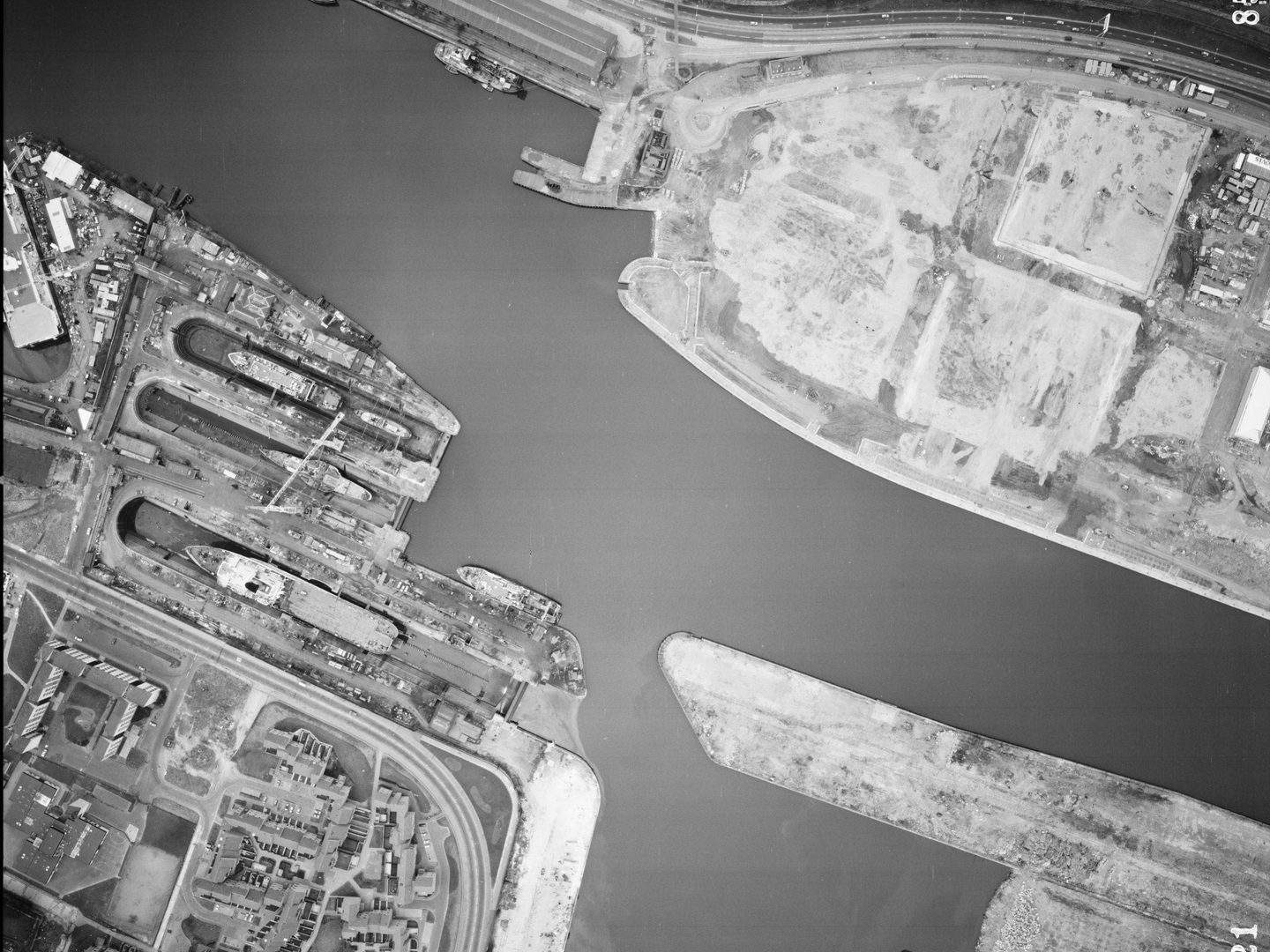 A large-scale black and white aerial photo of Glasgow. The river from the previous images now occupies almost the whole frame. At the left side, ships are clearly visible docked next to the river. There are blocks of flats in the bottom left corner.