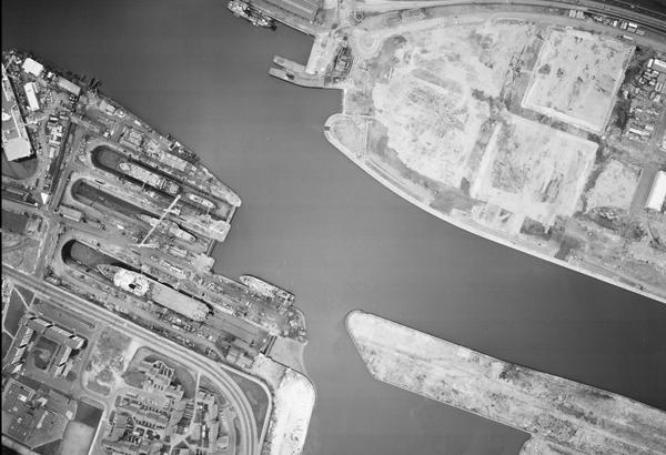 A large-scale black and white aerial photo of Glasgow. The river from the previous images now occupies almost the whole frame. At the left side, ships are clearly visible docked next to the river. There are blocks of flats in the bottom left corner.