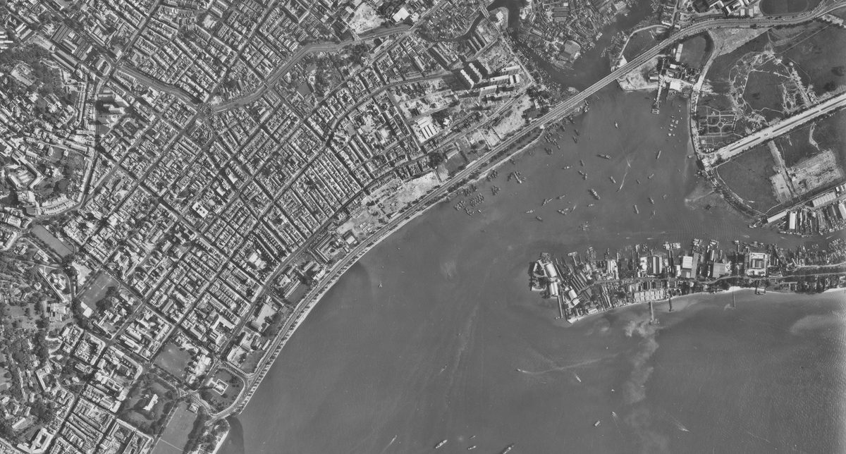 A historic black and white vertical aerial photo of a densely packed city. The sea is visible in the bottom right corner heavily dotted with vessels.