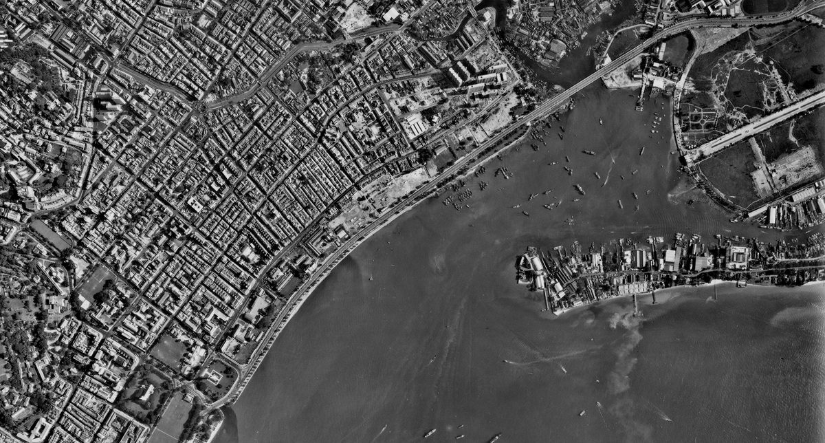 A historic black and white vertical aerial photo of a densely packed city. The sea is visible in the bottom right corner heavily dotted with vessels.