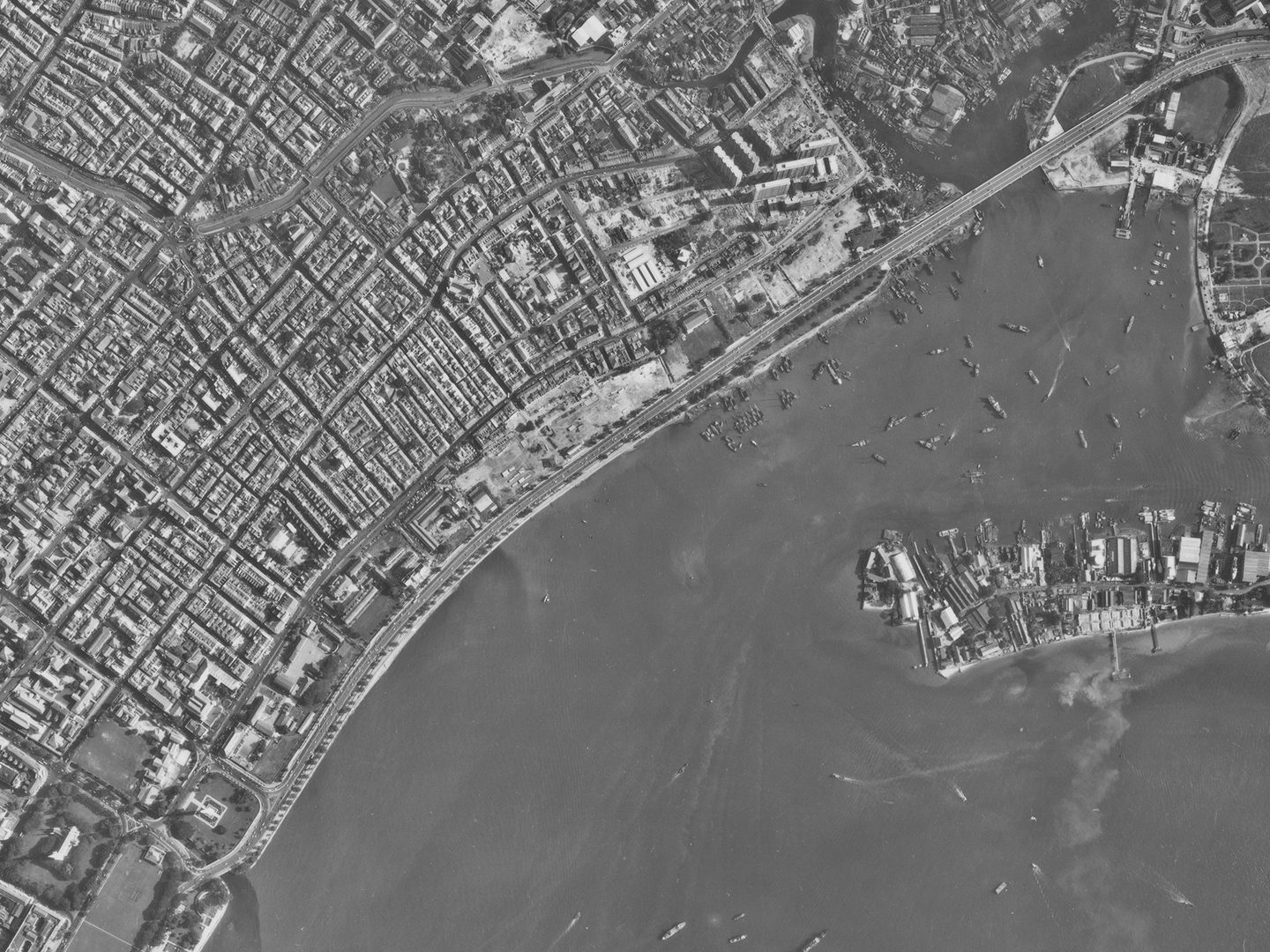 A historic black and white vertical aerial photo of a densely packed city. The sea is visible in the bottom right corner heavily dotted with vessels.