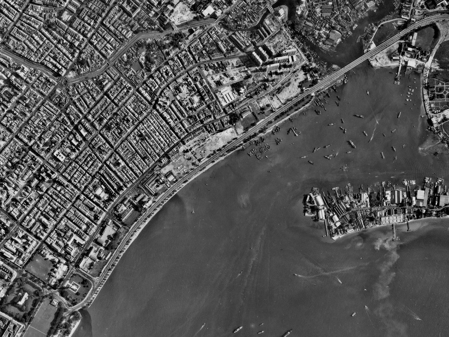 A historic black and white vertical aerial photo of a densely packed city. The sea is visible in the bottom right corner heavily dotted with vessels.