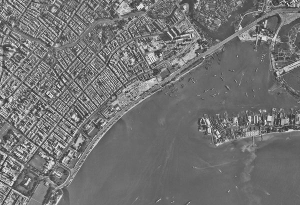 A historic black and white vertical aerial photo of a densely packed city. The sea is visible in the bottom right corner heavily dotted with vessels.