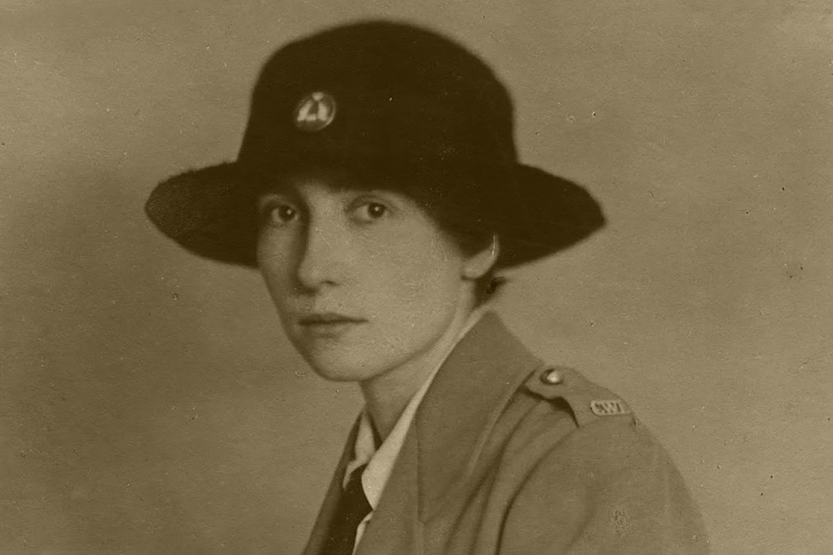A sepia historic photo of a young woman in uniform, wearing a wide-brimmed black hat and looking at the viewer.