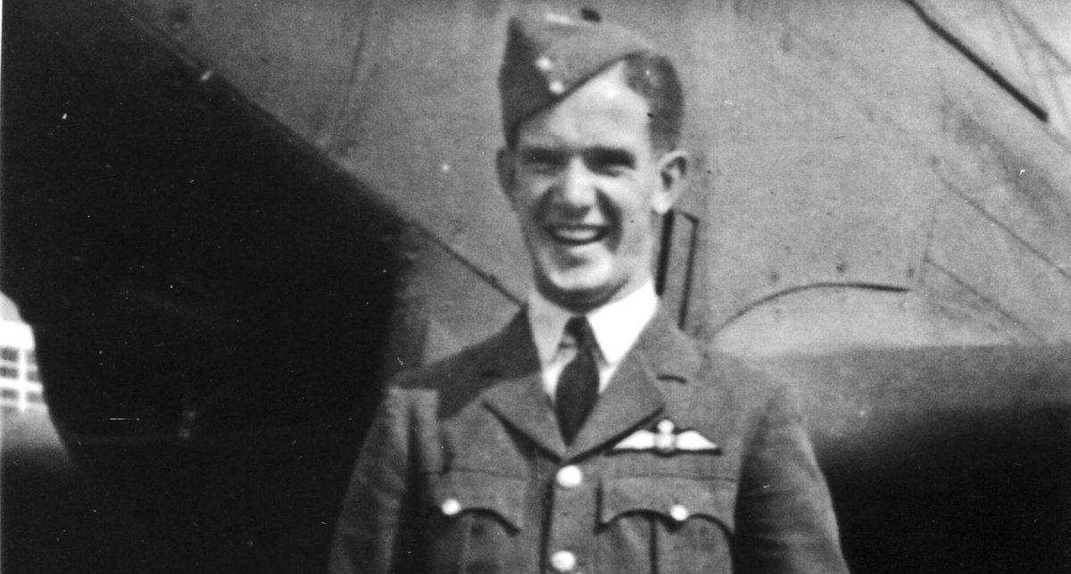 A historic sepia-coloured photo of a smiling man in uniform. He wears a beret and has an RAF wings badge on his left breast. He is standing in front of an aircraft.