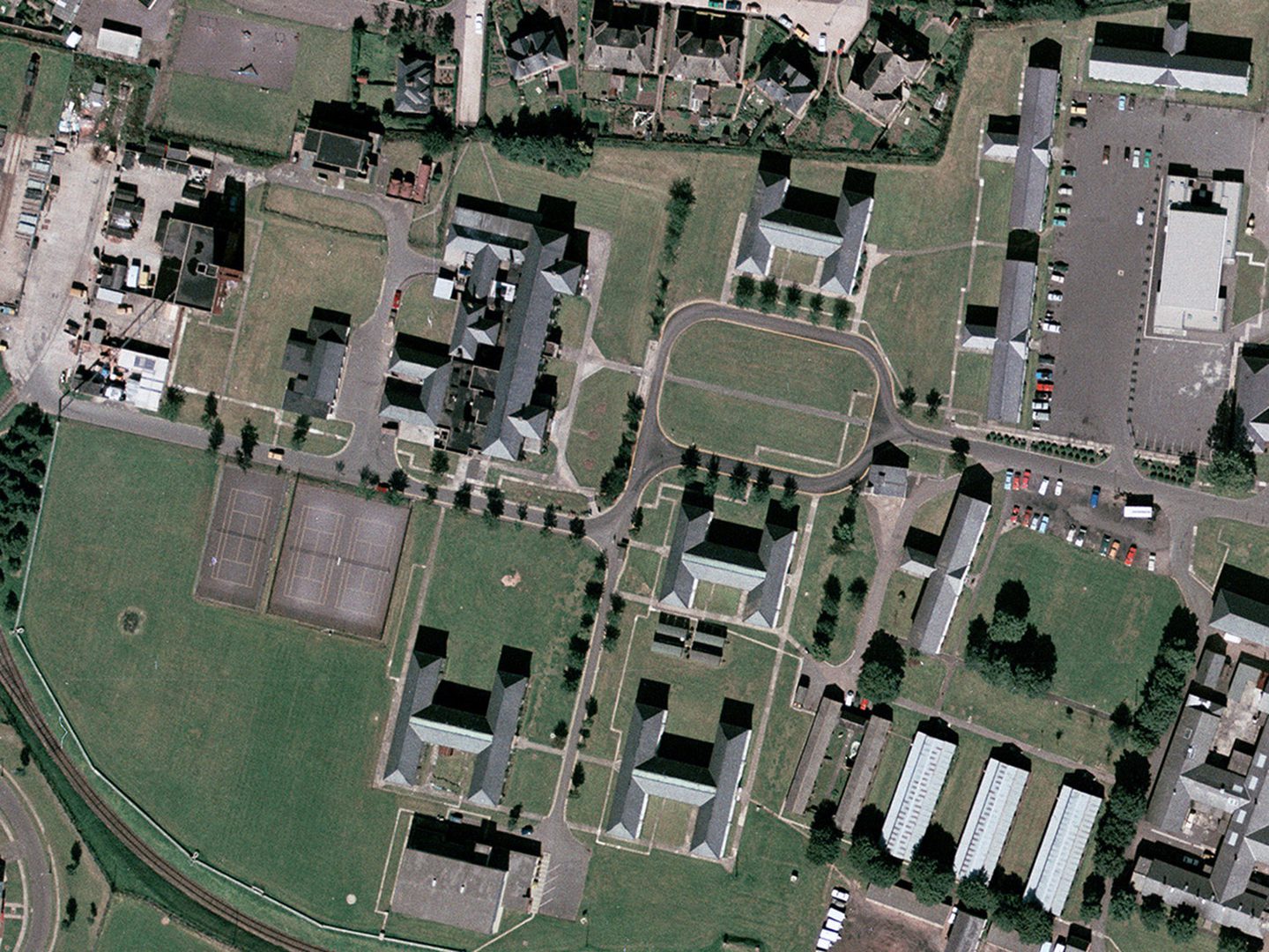 A historic colour vertical aerial photo of several H and L shaped buildings, linked by roads and surrounded by green spaces. To the top right is a car park.
