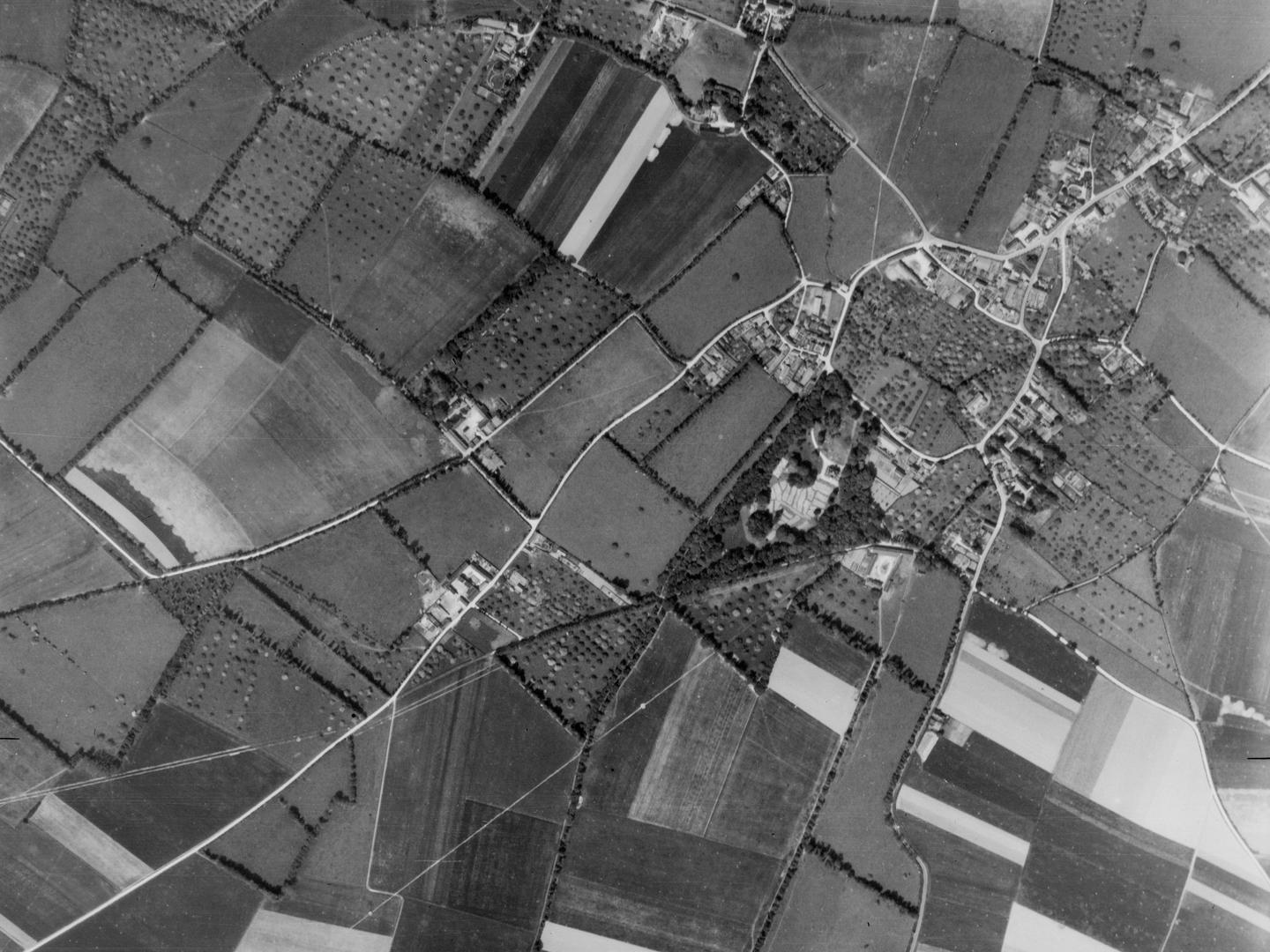 A black and white vertical aerial photo of a network of lanes and fields, with a small village visible to the right.