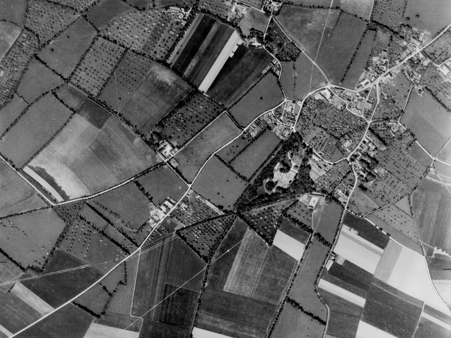 A black and white vertical aerial photo of a network of lanes and fields, with a small village visible to the right.