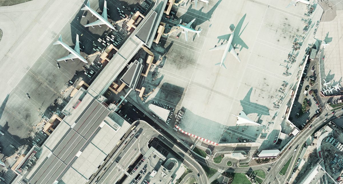 A historic colour vertical aerial photo of an airport. Airport buildings and numerous aircraft are visible, including three large airliners and a Concorde. The low light means the Concorde is throwing a dramatic shadow of itself.
