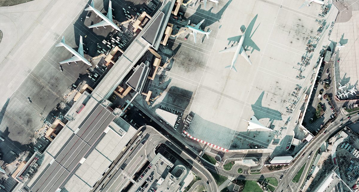 A historic colour vertical aerial photo of an airport. Airport buildings and numerous aircraft are visible, including three large airliners and a Concorde. The low light means the Concorde is throwing a dramatic shadow of itself.
