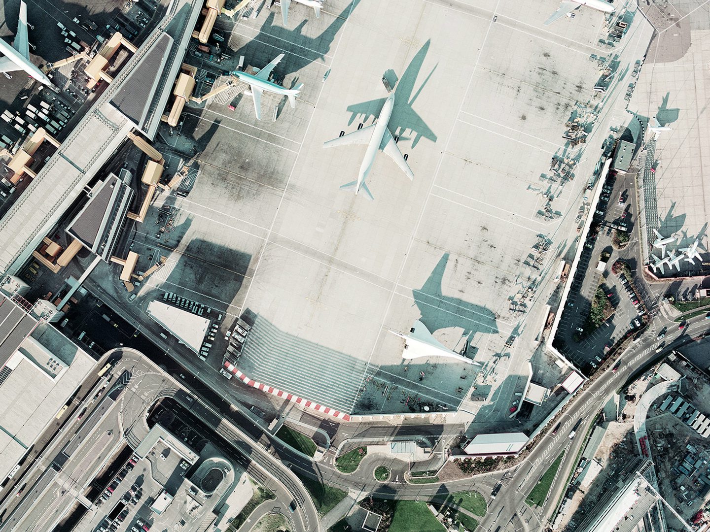 A historic colour vertical aerial photo of an airport. Airport buildings and numerous aircraft are visible, including three large airliners and a Concorde. The low light means the Concorde is throwing a dramatic shadow of itself.