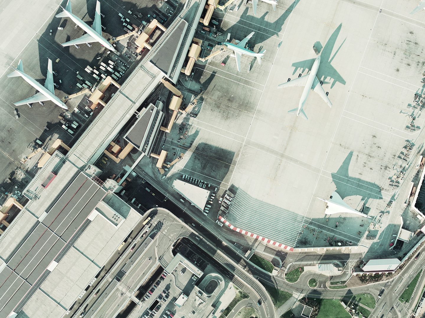 A historic colour vertical aerial photo of an airport. Airport buildings and numerous aircraft are visible, including three large airliners and a Concorde. The low light means the Concorde is throwing a dramatic shadow of itself.