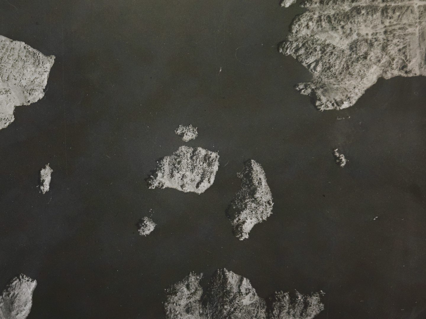 A historic black and white vertical aerial photo of several rocky islands surrounded by dark water.