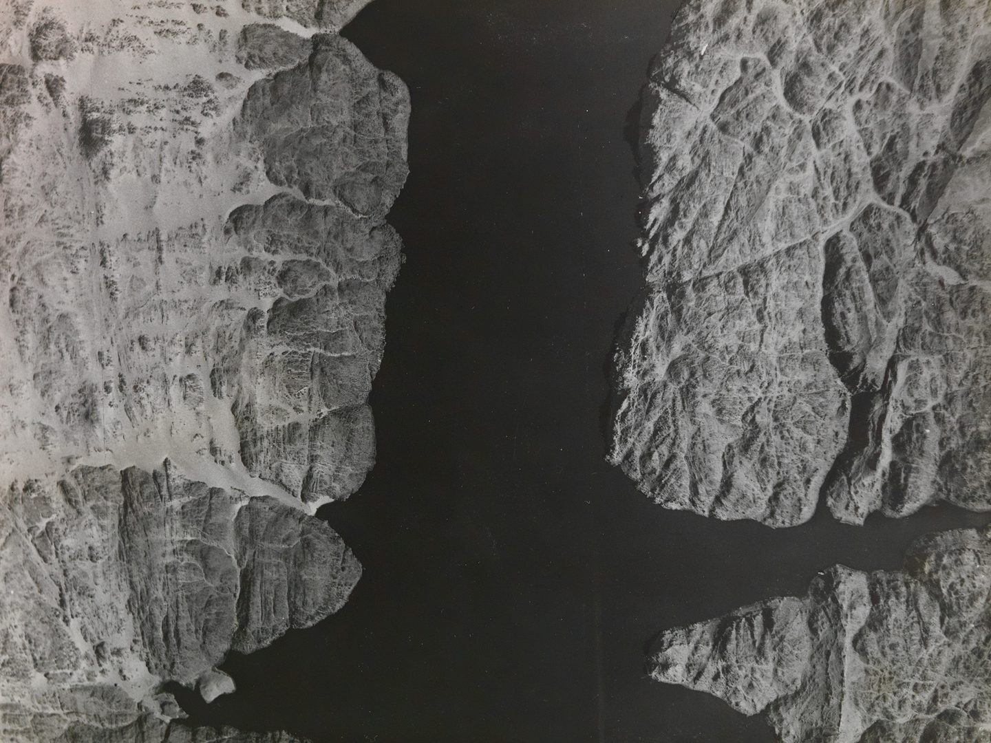A historic black and white vertical aerial photo of a wide river with fissured rocky banks. The river runs from the top of the image to the bottom, with the banks at the right and left sides.