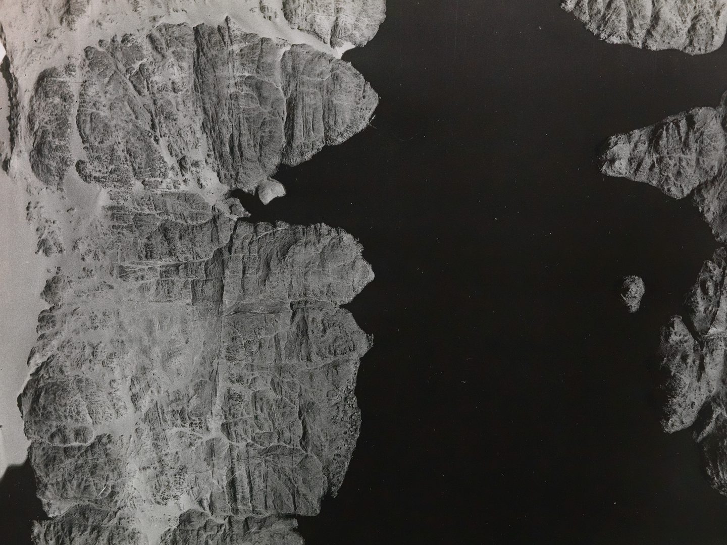 A historic black and white vertical aerial photo of a rive running alongside a fissured rocky bank. The river runs from the top of the image to the bottom, with the bank on the left-hand side.