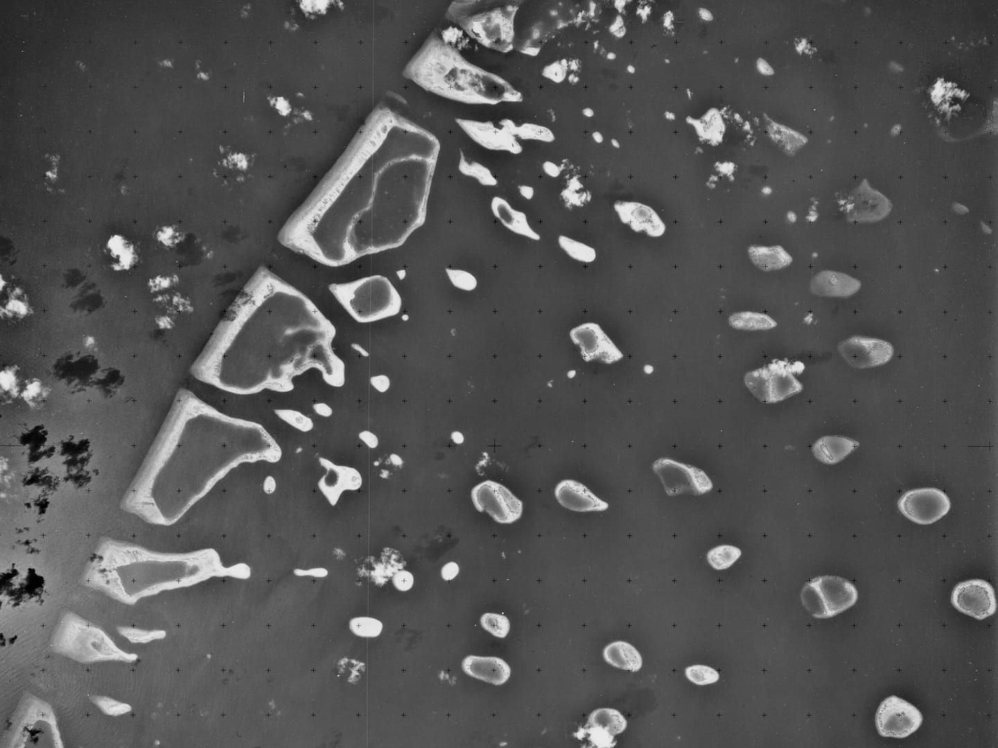 A black and white vertical aerial photo of numerous sandy islands scattered across the sea.