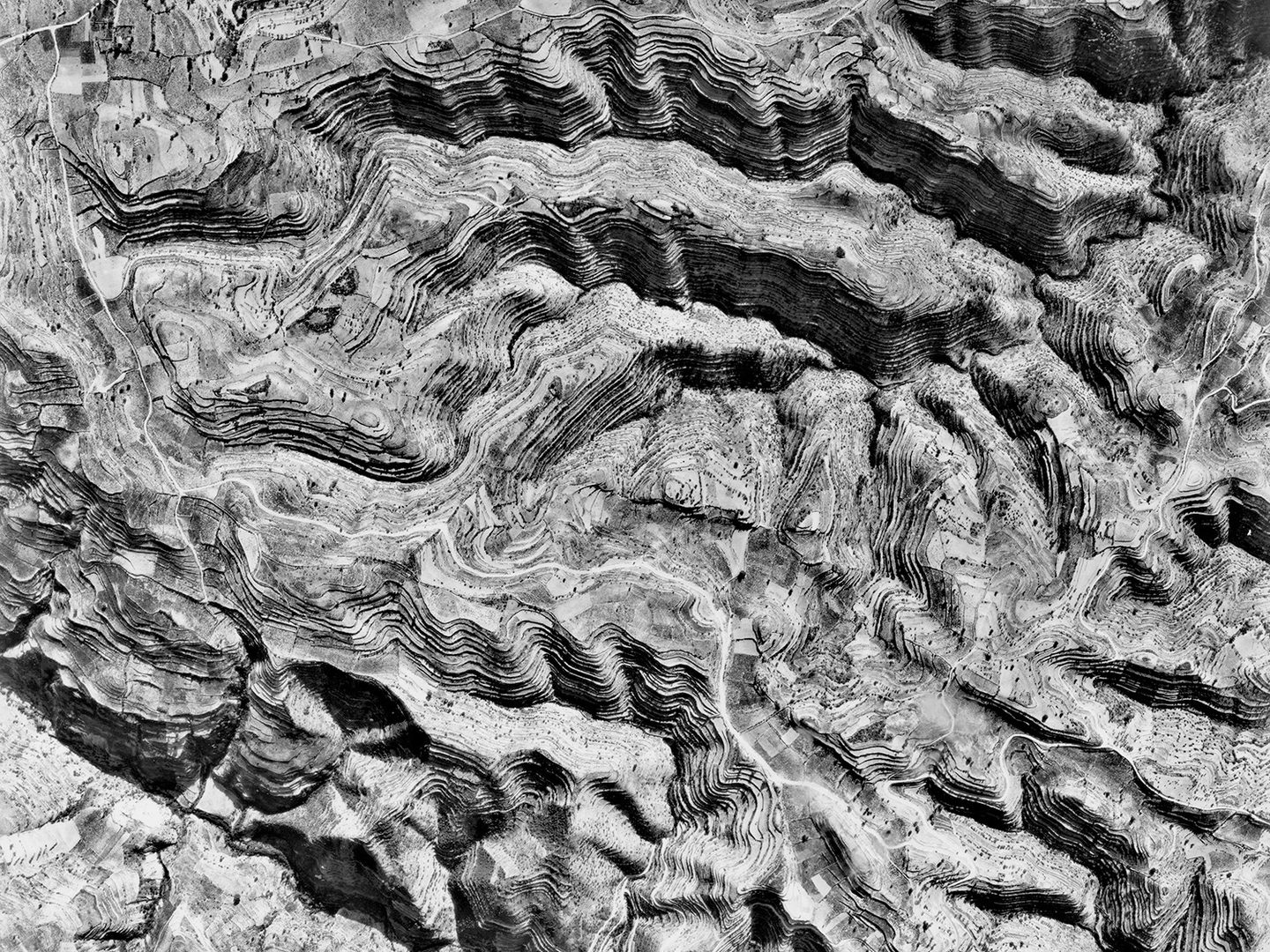 A black and white vertical aerial photo of a landscape. A complex network of hills and valleys crosses the landscape. The hills are very heavily terraced.