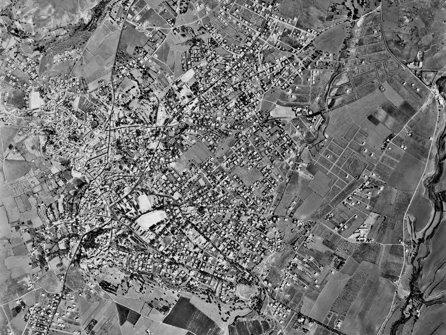 A historic black and white vertical aerial photo of an irregularly shaped town surrounded by fields.