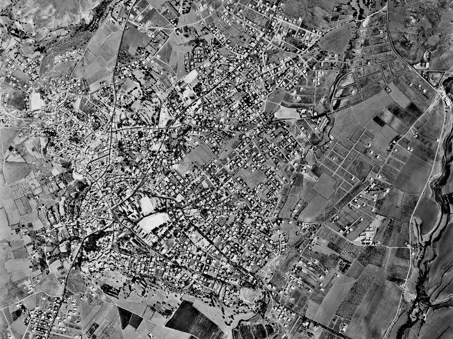 A historic black and white vertical aerial photo of an irregularly shaped town surrounded by fields.