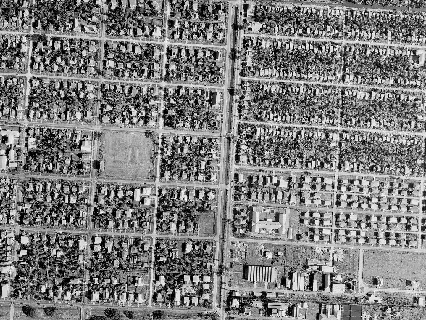 A historic black and white vertical aerial photo of a city. Houses are arranged in neat blocks, interspersed with trees.