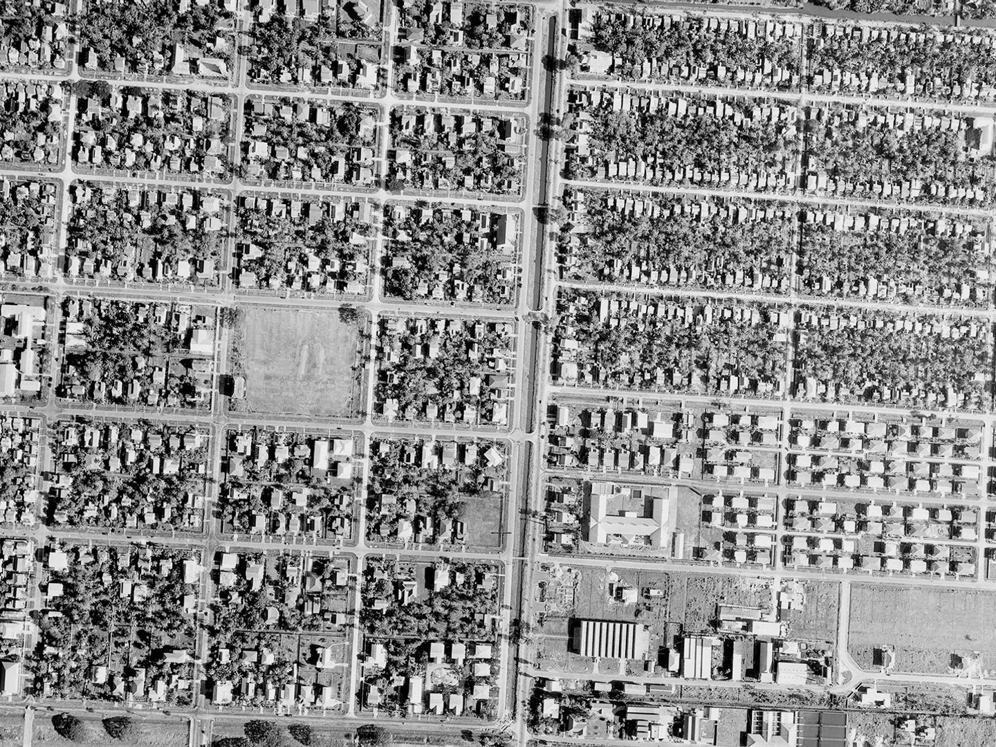 A historic black and white vertical aerial photo of a city. Houses are arranged in neat blocks, interspersed with trees.