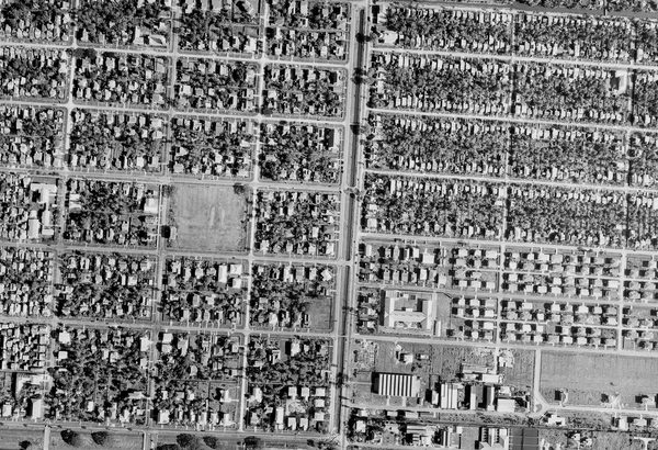 A historic black and white vertical aerial photo of a city. Houses are arranged in neat blocks, interspersed with trees.