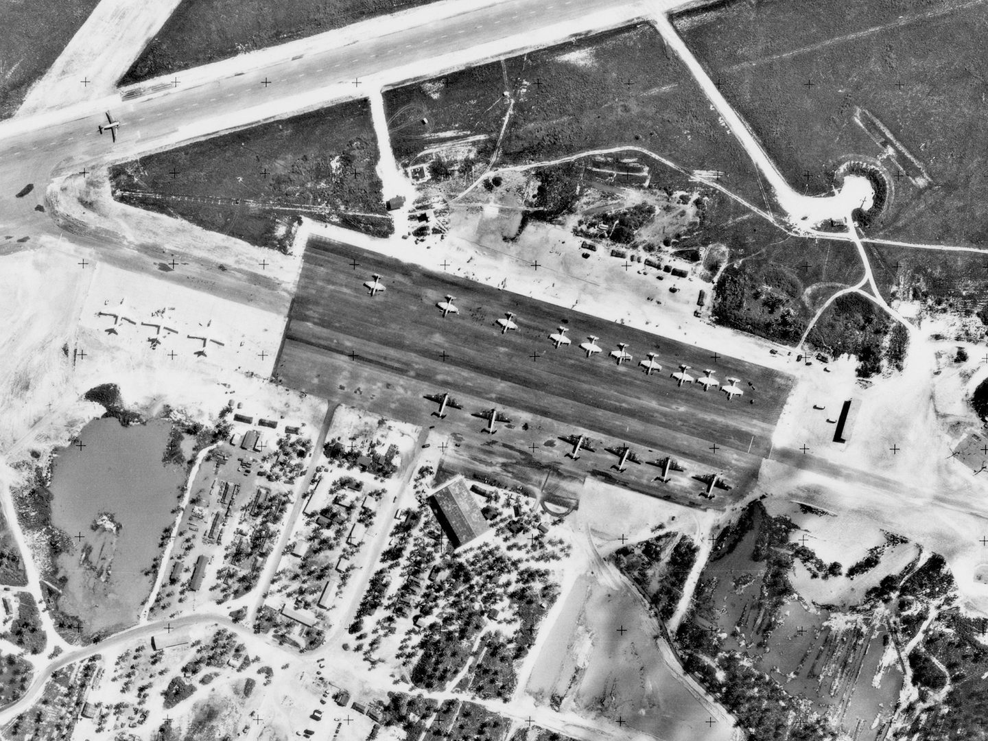 A historic black and white vertical aerial photo of an airfield. 19 aircraft are parked on a large area of concrete in the middle of the image: 3 Valiants, 6 Shackletons and 10 Canberras. Buildings among trees surround the parking area.