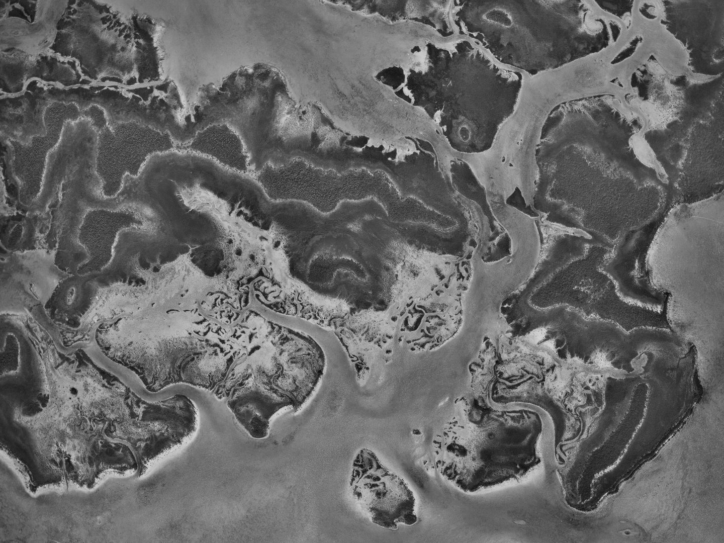 A black and white vertical aerial photo of a complex island coastline surrounded by sea.