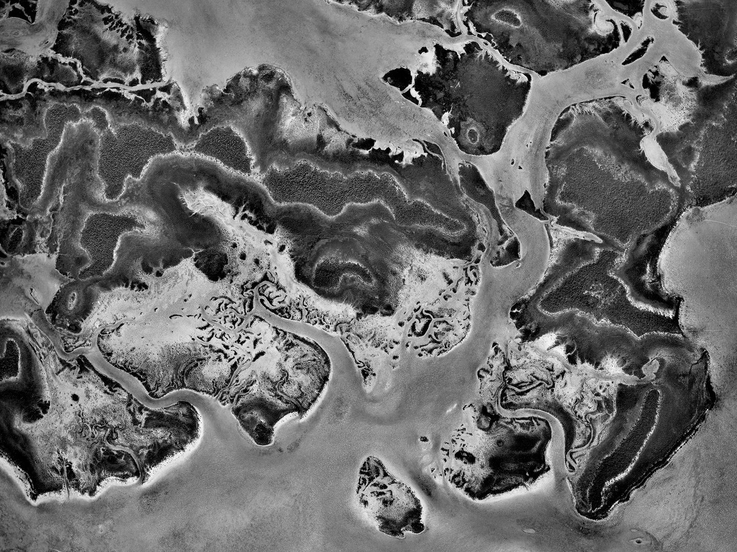 A black and white vertical aerial photo of a complex island coastline surrounded by sea.