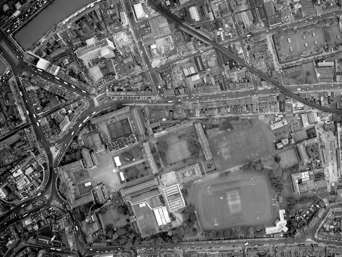 A historic black and white vertical aerial photo of the city of Dublin. To the left are several groups of buildings arranged around courtyards. They form the shape of a Greek cross. To their left are several playing fields.