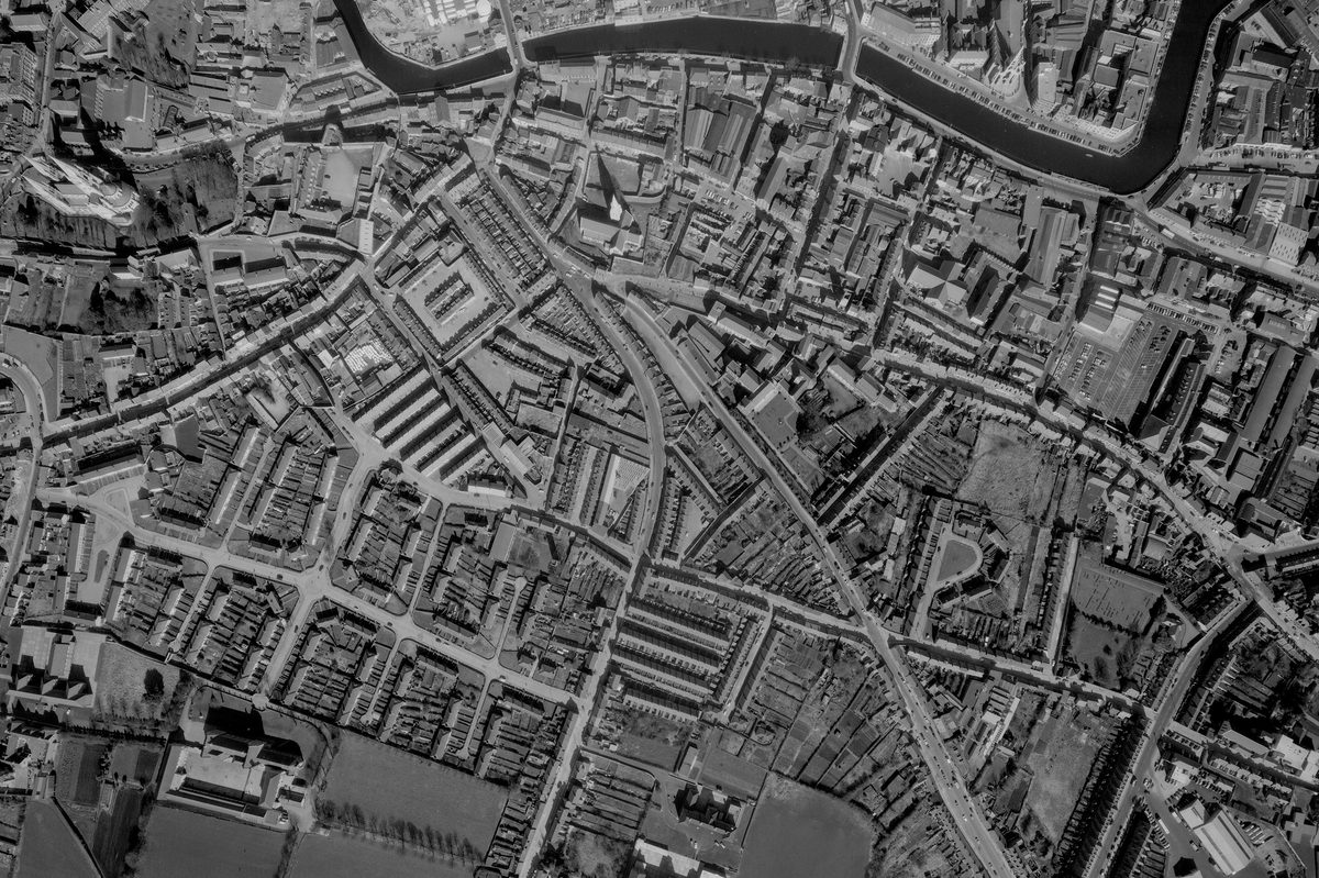 A historic black and white vertical aerial photo of a city grid, with a river running along the top edge of the image.