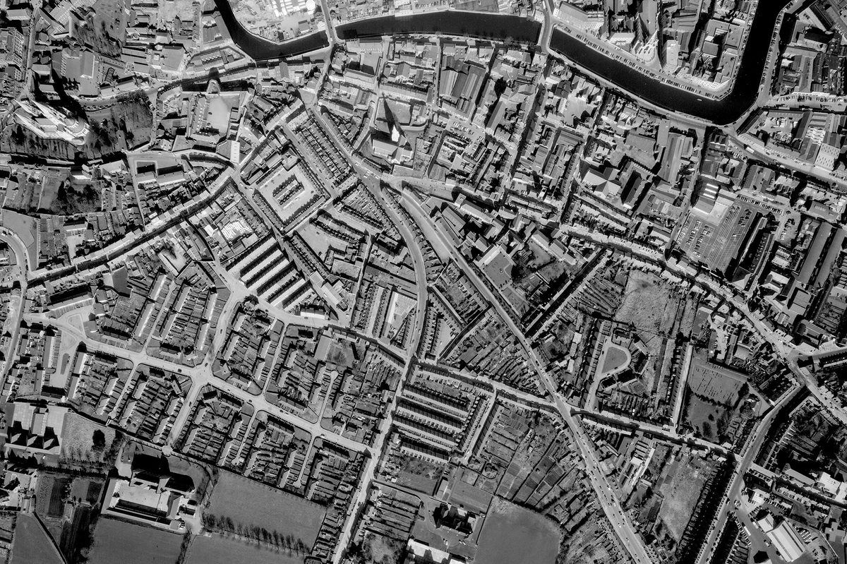 A historic black and white vertical aerial photo of a city grid, with a river running along the top edge of the image.