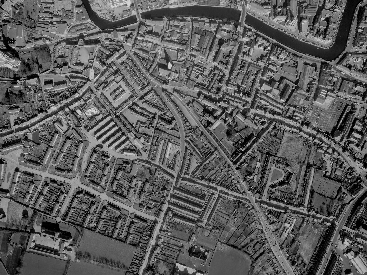 A historic black and white vertical aerial photo of a city grid, with a river running along the top edge of the image.