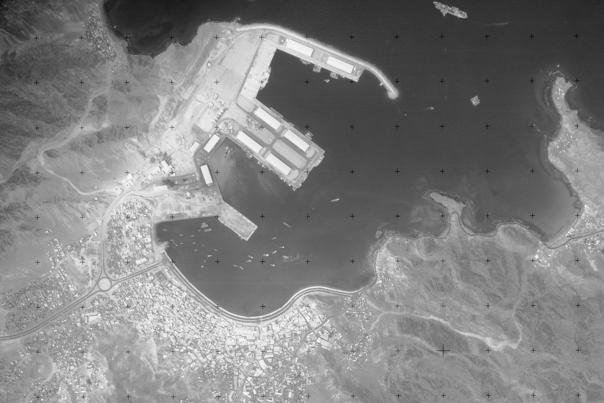 A historic black and white vertical aerial photo of a city on the coast. The city is situated on a large natural inlet. Along the left-hand shore of the inlet a large port is visible. The sea is at the top of the image, with several vessels visible on it.