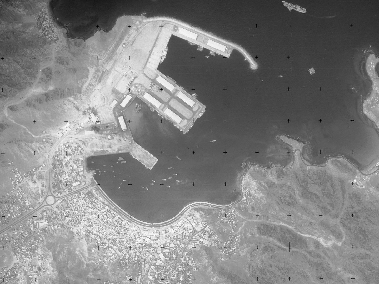 A historic black and white vertical aerial photo of a city on the coast. The city is situated on a large natural inlet. Along the left-hand shore of the inlet a large port is visible. The sea is at the top of the image, with several vessels visible on it.