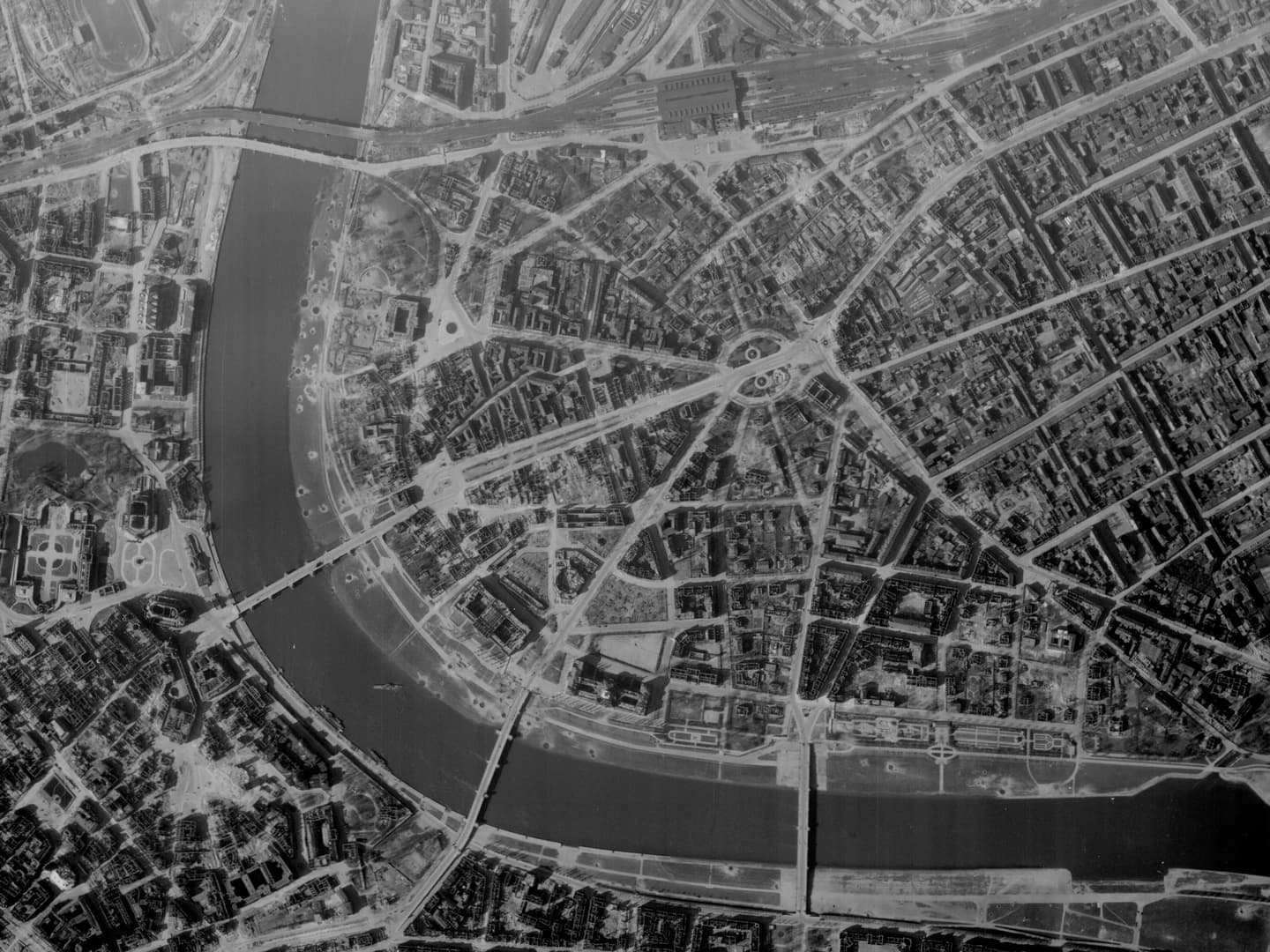 A black and white vertical aerial photo of Dresden. A wide river curves along the left and bottom edges, crossed by 4 bridges. Bomb damage is visible in roofless houses and craters.