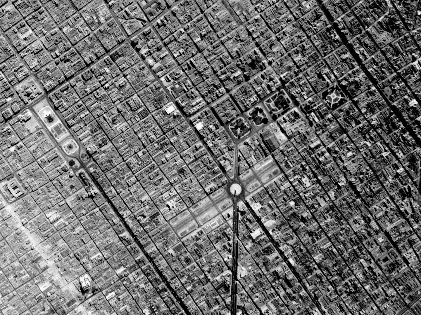 A historic black and white vertical aerial photo of a large city broken up into a regular grid. Just below right of the centre is a monument in the middle of a wide boulevard.