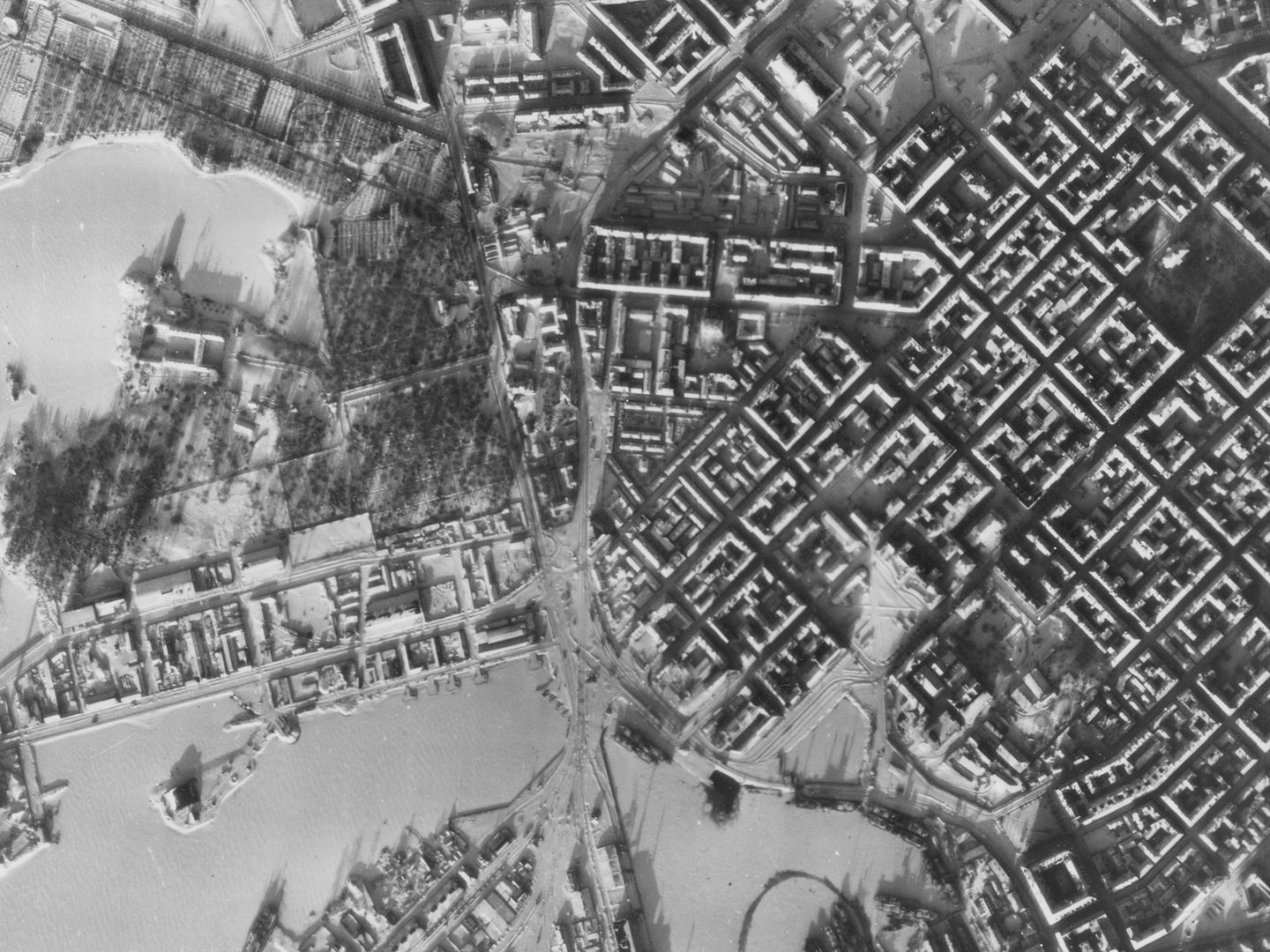 A historic black and white vertical aerial photo of Helsinki in winter. The regular grid of streets stands out against the snow. To the left is a ragged coastline fringed by frozen sea.