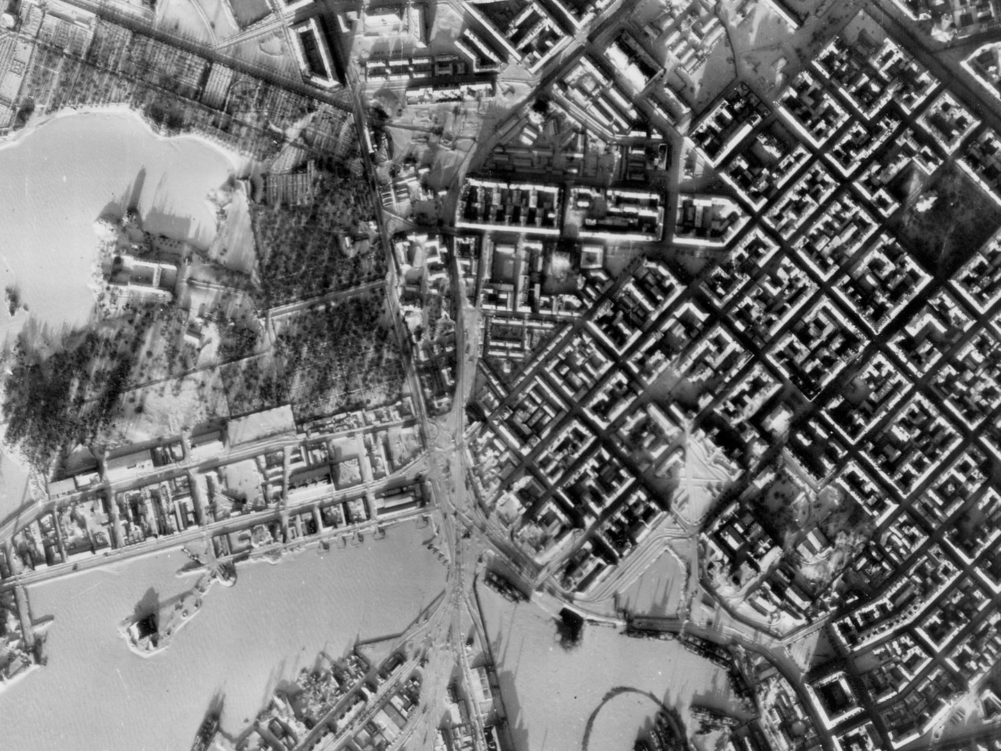 A historic black and white vertical aerial photo of Helsinki in winter. The regular grid of streets stands out against the snow. To the left is a ragged coastline fringed by frozen sea.