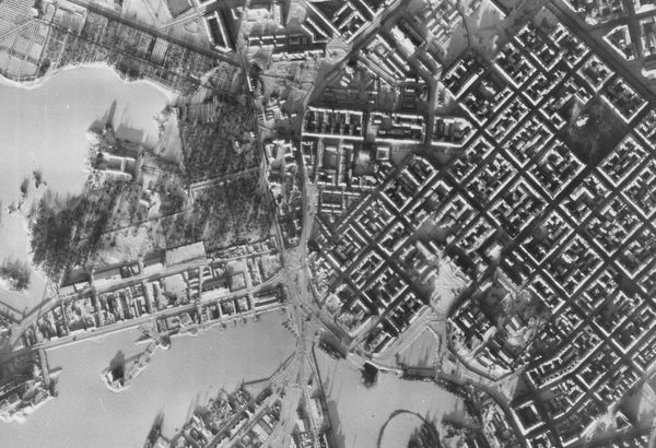 A historic black and white vertical aerial photo of Helsinki in winter. The regular grid of streets stands out against the snow. To the left is a ragged coastline fringed by frozen sea.