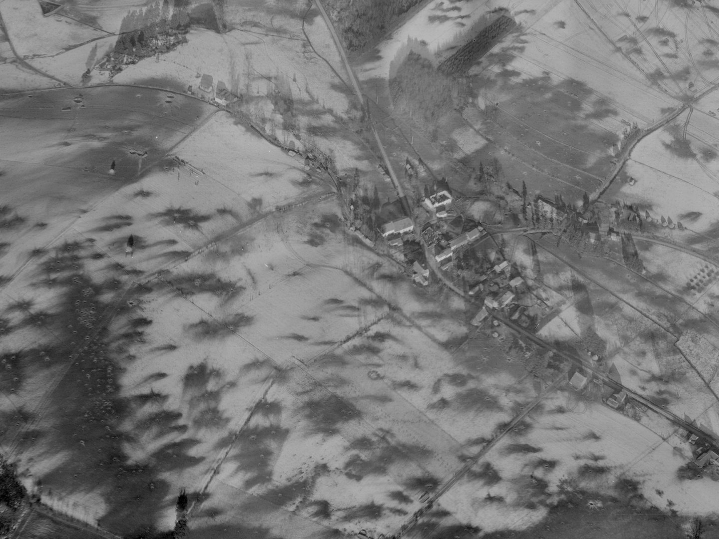 A historic black and white oblique aerial photo of a small village. The village and surrounding fields are covered with snow. Numerous bomb craters mark the snowy fields.